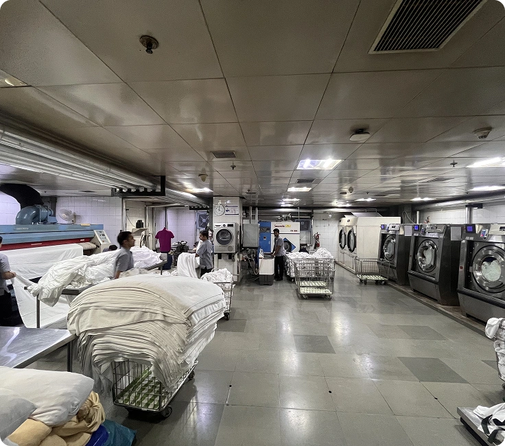 Wide view of complete in-house laundry facility with flatwork ironer, washer extractors, and laundry staff at Holiday Inn Aerocity, New Delhi