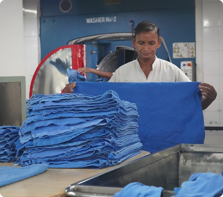 Medanta Hospital Gurugram Laundry Staff Folding Processed Surgical Scrubs Next To Industrial Washer Extractor