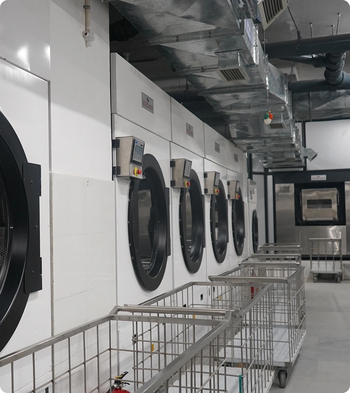 Row of Supershine tumble dryers with linen trolleys at Lady Hardinge Medical College and Hospital's in-house laundry facility, New Delhi