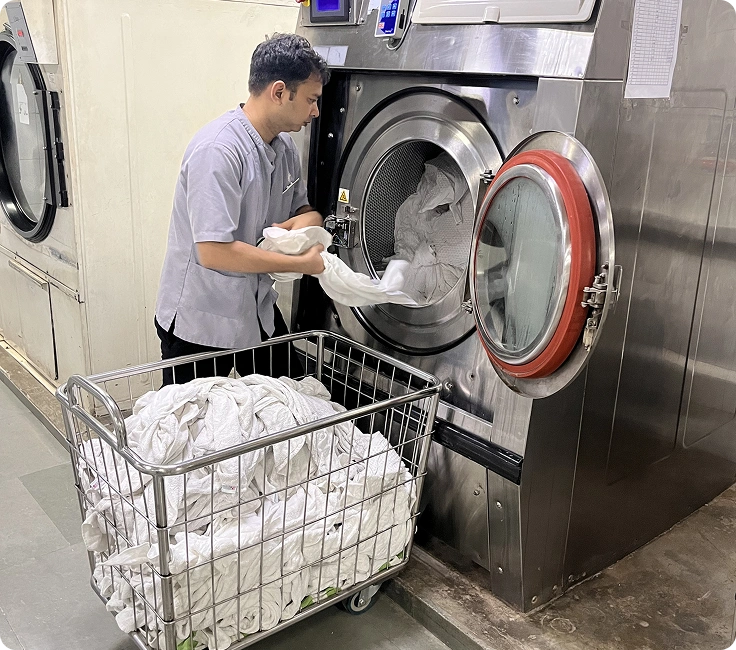 Operator loading hotel linen into washer extractor at Holiday Inn Aerocity's in-house laundry facility, New Delhi